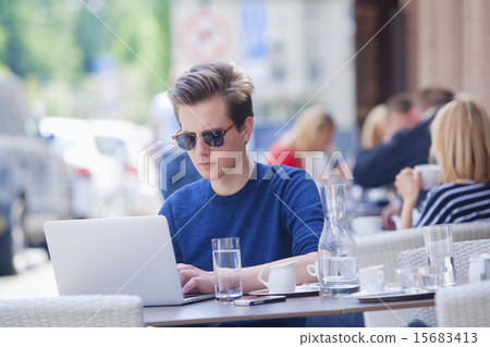 Young Man with Laptop Sitting in Outside Coffeehouse 15683413