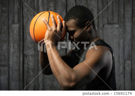 Afro-american basketball player pressing ball to his forehead 15691174