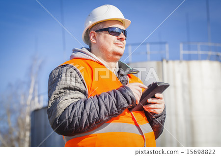 Engineer with tablet PC with oil tank in the backg 15698822