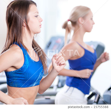Two young women run on machine in the gym 15755388