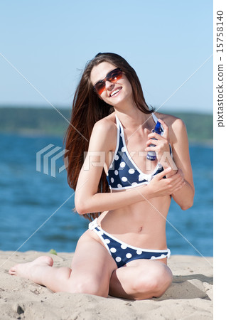 Beautiful woman applying suntan lotion at beach 15758140