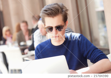 Young Man with Laptop Sitting in Outside Coffeehouse Young Man with Laptop Sitting in Outside Coffeehouse 15784390