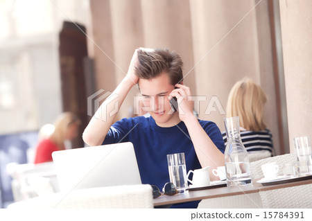 Young Man Sitting in Outside Coffeehouse Talking on Phone Young Man Sitting in Outside Coffeehouse Talking on Phone 15784391