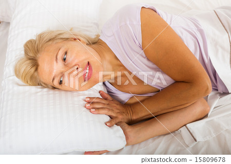 mature woman in shirt laying on bed at bedroom 15809678