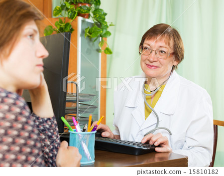 Mature doctor behind computer with patient Mature doctor behind computer with patient 15810182