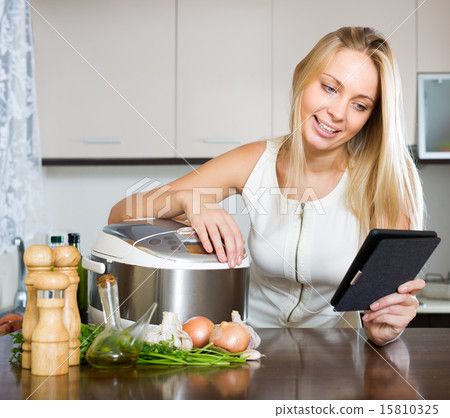 Woman reading ereader near multicooker 15810325