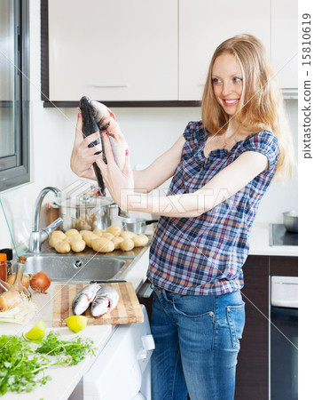 Smiling blonde girl cooking seabass fish Smiling blonde girl cooking seabass fish 15810619