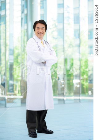 Full-body image of middle-aged male doctor standing at entrance of general hospital Full-body image of middle-aged male doctor standing at entrance of general hospital 15865614