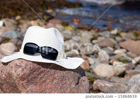 White straw hat with sunglasses lies on a big rock 15868639