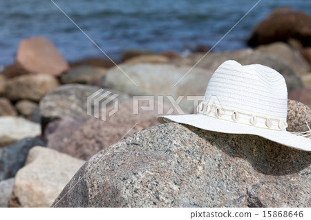 An white straw hat lies on a rock on the beach An white straw hat lies on a rock on the beach 15868646