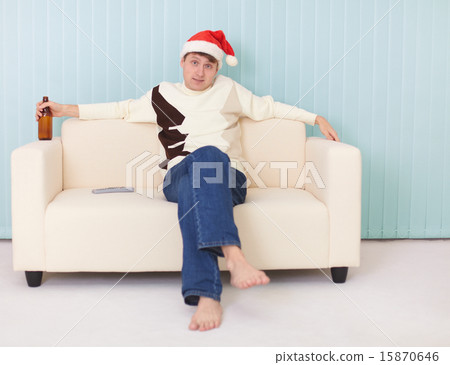 Man in a New Year's cap sits on sofa with bottle Man in a New Year's cap sits on sofa with bottle 15870646