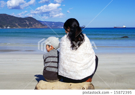 Parent and child sitting on driftwood on the beach 15872395