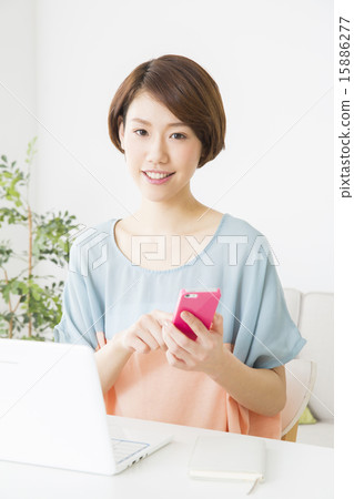 一位在個人電腦前操作智能手機的年輕女士 15886277