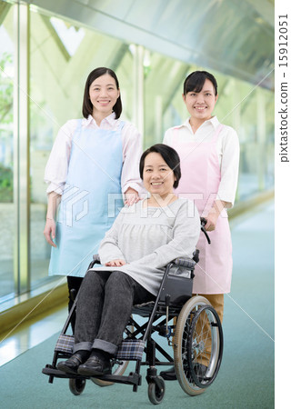 在走廊的走廊的兩位女性幫手走設施的婦女的圖像輪椅的 15912051