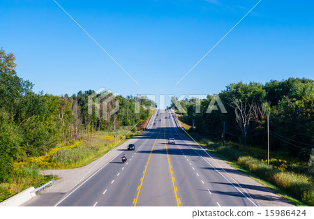 Wide road with few cars by forest 15986424