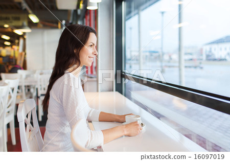 smiling young woman drinking coffee at cafe 16097019