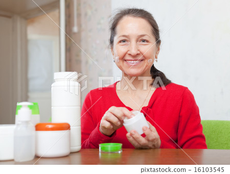Happy mature woman puts cream on face 16103545
