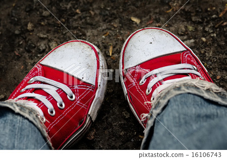 Feet in dirty red sneakers and jeans outdoors. Feet in dirty red sneakers and jeans outdoors. 16106743