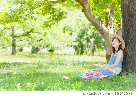A woman sitting and resting in the shade of the early summer park 16142576