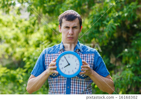 man holding a clock with both hands on a green background Summ man holding a clock with both hands on a green background Summ 16168302