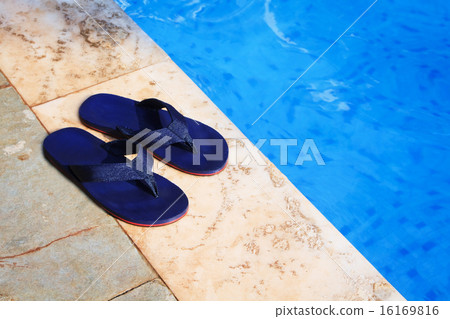 pair of blue flip flops at the edge of a swimming pool pair of blue flip flops at the edge of a swimming pool 16169816