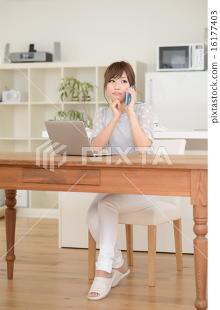 一位年輕的女士用智能手機打電話·一台筆記本電腦 一位年輕的女士用智能手機打電話·一台筆記本電腦 16177403