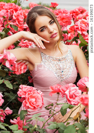 Pretty woman is sitting in bush of pink roses  16199073