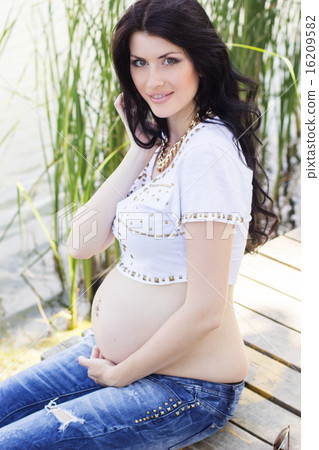 Pregnant brunette girl sitting on bridge near river Pregnant brunette girl sitting on bridge near river 16209582