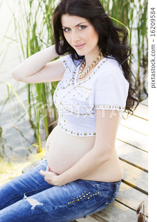 Pregnant brunette woman sitting on bridge near river 16209584