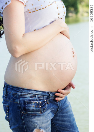 Belly of pregnant girl sitting on bridge near river Belly of pregnant girl sitting on bridge near river 16209585