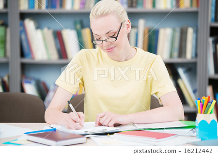 Happy student with glasses writing in library Happy student with glasses writing in library 16212442