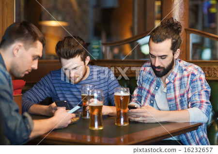 male friends with smartphones drinking beer at bar 16232657