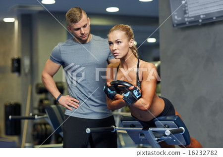 woman with personal trainer flexing muscles in gym 16232782