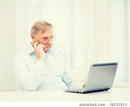 old man in eyeglasses working with laptop at home 16232813