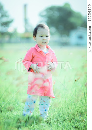 Child walking happily in grass field with pink 16254309