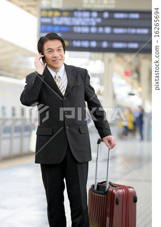 An image of a businessman in his 50s who has a carry bag and is calling at the bullet train home An image of a businessman in his 50s who has a carry bag and is calling at the bullet train home 16265694