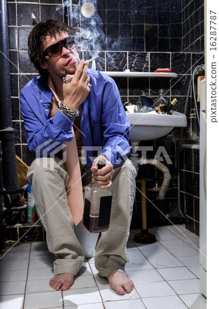 Drunk Man sits in a toilet with a bottle of whiskey and smoking Drunk Man sits in a toilet with a bottle of whiskey and smoking 16287787