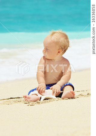 Portrait of child playing with sea shell on beach 16336858