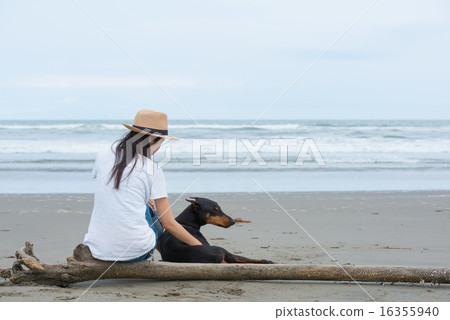 A woman sitting on a beach with a dog 16355940