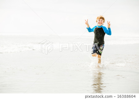 Young boy in swimming shorts and rash vest runs along Bali beach near sunset Young boy in swimming shorts and rash vest runs along Bali beach near sunset 16388604