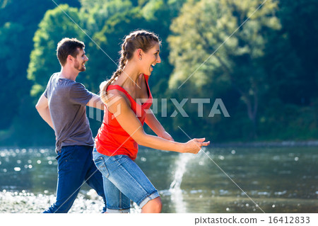 Man and woman skimming stones on river 16412833