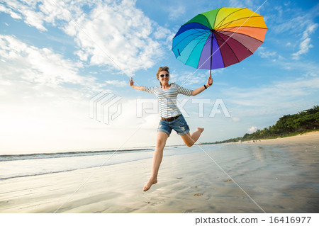 Cheerful young girl with rainbow umbrella having fun on the beach before sunset. Travel, holidays Cheerful young girl with rainbow umbrella having fun on the beach before sunset. Travel, holidays 16416977