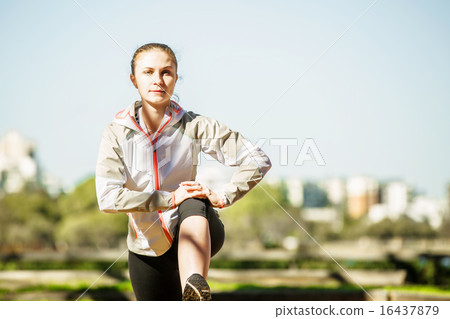Young fit girl stretching out on bench before exercising in autumn pak with city at background Young fit girl stretching out on bench before exercising in autumn pak with city at background 16437879