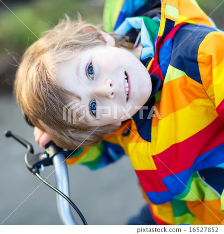 kid boy in safety helmet and colorful raincoat riding bike, outd kid boy in safety helmet and colorful raincoat riding bike, outd 16527852