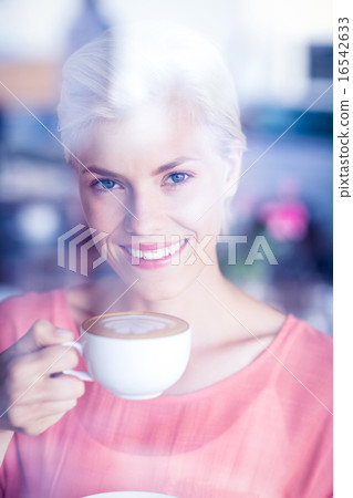 Happy blonde woman smiling at camera and holding a cup of coffee Happy blonde woman smiling at camera and holding a cup of coffee 16542633