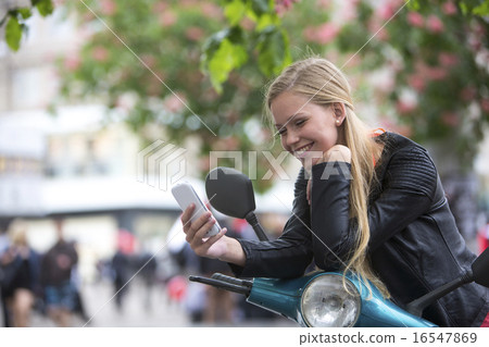 Cute, blond young woman on a scooter laughing 16547869