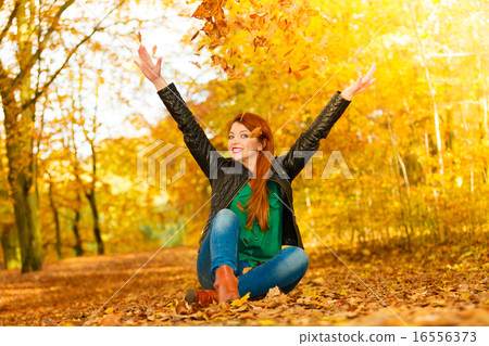 Girl relaxing in autumn park throwing leaves up in the air. 16556373