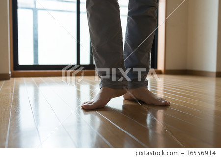 The feet of a man standing barefoot on a wooden floor. The feet of a man standing barefoot on a wooden floor. 16556914
