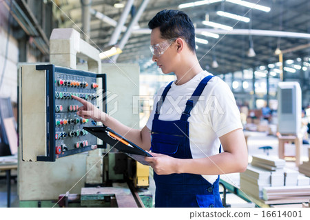 Worker pressing buttons on CNC machine in factory 16614001