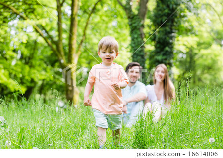 Little boy running over meadow with family in back 16614006